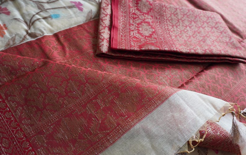 May include: A folded red textile with a gold floral pattern and a white border. The fabric is layered on top of a floral patterned surface. The textile has a luxurious appearance.
