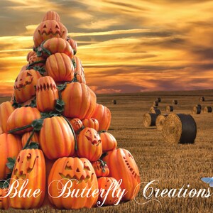 May include: A pile of orange pumpkins with carved faces, arranged in a pyramid shape, against a backdrop of a golden sunset over a field of hay bales. The text "Blue Butterfly Creations" is visible in the foreground.