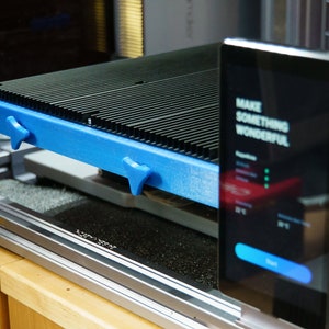 May include: A 3D printer with a blue platform and a black and silver body. The printer has a touchscreen display that says "Make something wonderful."