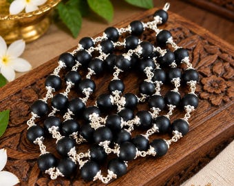 May include: A long necklace featuring matte black spherical beads separated by intricate silver-toned metal caps. The beads are linked together in a continuous chain, creating a textured, dark, and metallic appearance throughout the jewelry piece.
