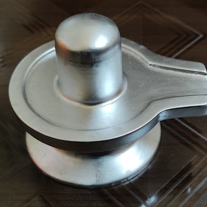 May include: A silver Shiva Lingam statue with a base and a crescent moon shape on the side. The statue is made of metal and has a smooth, polished finish.