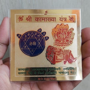 Puede incluir: Una tarjeta chapada en oro con una imagen de una deidad hindú y texto en sánscrito. El texto dice "Shri Kamakhya Yantra" y "Kamakhya Kasasampanna Kameshwari Harpriyami. Kamanaan Dehi Se Nitya Kameshwari Namostu Te.". La tarjeta está chapada en oro de 24 quilates.