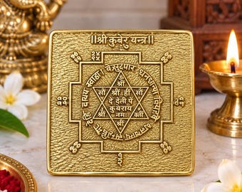 Puede incluir: Una placa cuadrada de metal color oro Kuber Yantra con intrincados patrones geométricos en relieve y escritura devanagari. La superficie tiene un acabado texturizado, con un diseño central de estrella de seis puntas con caracteres sánscritos.