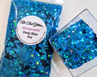 May include: A close-up of a small plastic bag filled with holographic blue glitter. The bag has a label that reads "All That Glitters... Holographic Deep Blue Sea www.AllThatGlitters2021.etsy.com".