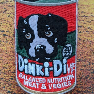 May include: Embroidered patch in the shape of a dog food can, featuring a black and white dog face. The can is red with green and white text that reads "Dinki-Dive" and "Balanced Nutrition Meat & Vegies". The patch includes the year "2022".