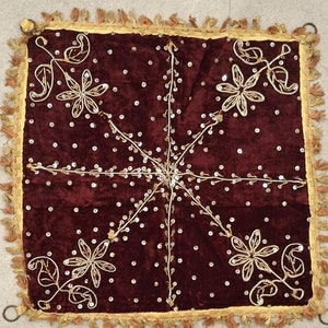 May include: A square, claret velvet textile with gold trim and fringe. The textile features embroidered floral designs and is embellished with small, scattered sequins. Metal rings are attached to each corner.