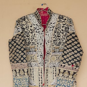 May include: A black and white embroidered jacket with a red lining and gold accents. The jacket is made from a patchwork of different fabrics and has a unique, bohemian style.