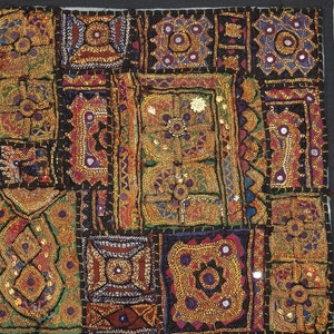 May include: A colourful patchwork quilt with intricate embroidery and mirror accents. The quilt is made of various fabrics in shades of brown, red, green, and blue. The quilt is edged with a black border.