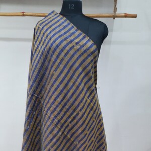 May include: A blue and gold striped kantha shawl with a fringed edge. The shawl is draped over a mannequin.