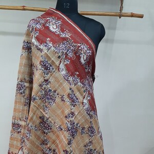 May include: A brown and beige patterned shawl with a red border. The shawl is draped over a mannequin.