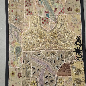 Peut inclure: Une tenture murale rectangulaire composée de panneaux de tissu beige en patchwork. L'ensemble est richement orné de fils métalliques dorés, de paillettes, de perles et de motifs floraux et cachemire brodés, encadré par une bordure en tissu noir.
