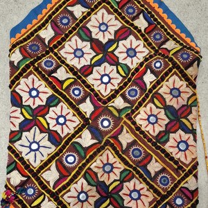 May include: A brown fabric bag with a colorful embroidered design featuring flowers and mirrors. The bag has a gold beaded strap and a blue and orange trim.