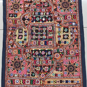 Può includere: Un arazzo da parete in patchwork colorato con ricami intricati e accenti a specchio. Il tessuto è un mix di marrone, rosso, arancione, blu, verde e giallo. Il design presenta forme e motivi geometrici.
