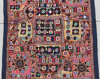 May include: A colorful patchwork wall hanging with intricate embroidery and mirror accents. The fabric is a mix of brown, red, orange, blue, green, and yellow. The design features geometric shapes and patterns.