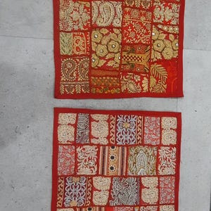 May include: Two red patchwork cushion covers with gold embroidery and embellishments. The covers are made of different fabrics and patterns, creating a unique and colorful design.