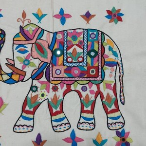 May include: A colorful embroidered elephant design on a white fabric background. The elephant is decorated with intricate patterns and flowers in various colors, including red, blue, green, yellow, and pink.
