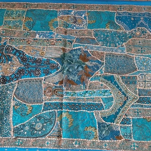 May include: A large, rectangular wall tapestry with a patchwork design. The tapestry is made of various fabrics in shades of blue, green, and brown. It is decorated with sequins and beads, creating a shimmering effect.