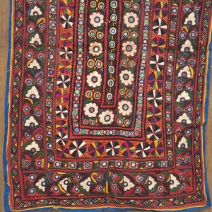 May include: A red fabric wall hanging with intricate embroidery and mirror work. The design features floral motifs, geometric patterns, and colorful threads.