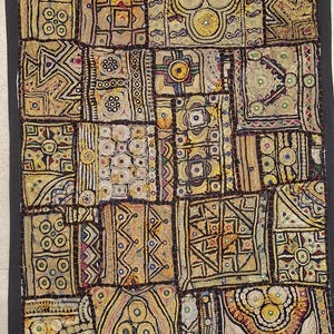 以下が含まれることがあります： ゴールド、ブラウン、ブラックの色合いで刺繍された布地の正方形をパッチワークした長方形の壁掛け。テキスタイル全体に、複雑な幾何学模様、円形のモチーフ、小さな反射する鏡のアクセントが施されています。