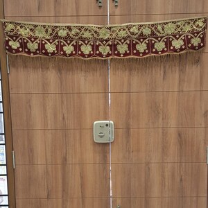 May include: A burgundy and gold door swag with a fringe trim. The swag has a floral design with gold sequins and butterflies.