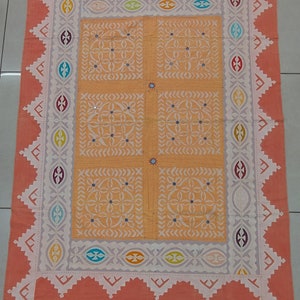May include: A hand-stitched quilt with a peach-coloured background and a white geometric pattern. The quilt has a decorative border with colourful accents.