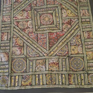 May include: A rectangular textile with a geometric pattern. The design features squares, rectangles, and diamond shapes filled with intricate floral and paisley motifs in red, yellow, and blue. The border is black.