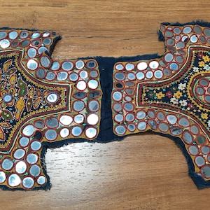May include: Two pieces of fabric featuring intricate embroidery and mirror work. The fabric is dark blue with gold, red, and white accents. The mirror pieces are round and have a silver finish.