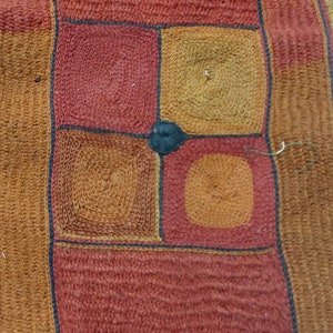 May include: Textile with a repeating pattern of squares and rectangles in shades of red, orange, and brown. The squares have a spiral design in the center, and the edges are outlined in black. The textile appears to be handmade.