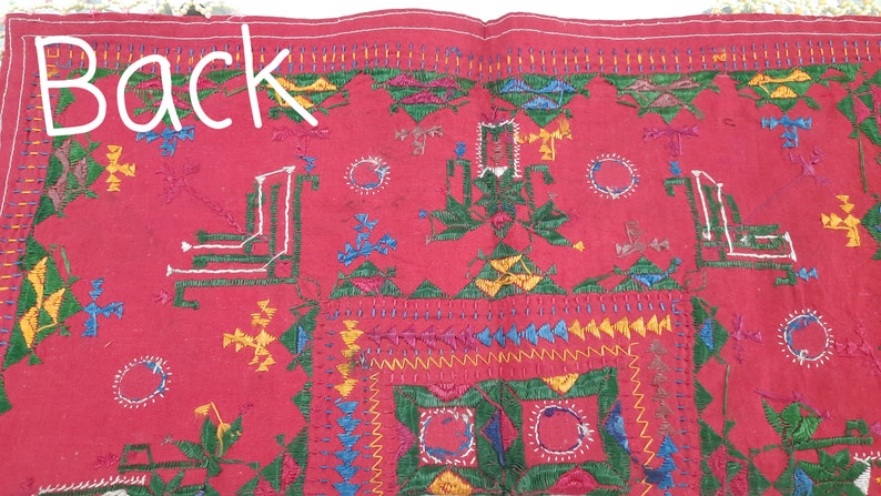 Pu&ograve; includere: Tessuto rosso con ricami intricati in verde, giallo, blu e bianco. La parola "Back" &egrave; scritta in bianco. Il design presenta forme geometriche e motivi floreali, mostrando una lavorazione artigianale dettagliata.