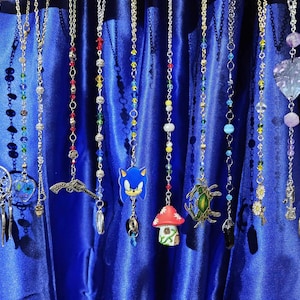 May include: A collection of 10 colorful beaded car charms with various pendants, including a dreamcatcher, a gun, a mushroom, a cartoon character, a turtle, a flower, a crystal, and a tree.