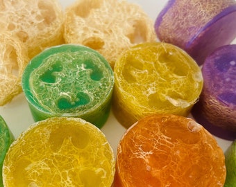 May include: Assortment of colorful loofah soap bars. The bars are round and have a textured surface. The colors include green, yellow, orange, and purple.