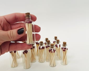 May include: A group of small glass bottles filled with wooden matches with red tips. The bottles have cork stoppers.