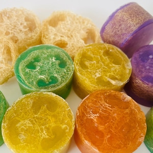 May include: Assortment of colorful loofah soap bars. The bars are round and have a textured surface. The colors include green, yellow, orange, and purple.