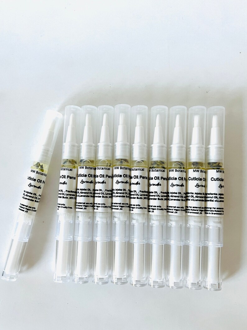 May include: A collection of clear cuticle oil pens with white caps, labeled "MW Botanical Cuticle Oil Pen Lavender." The pens are filled with a light yellow liquid and are arranged on a white surface.