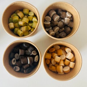 May include: Four paper cups filled with different colored candy. The cups are arranged in a square pattern on a white surface. The candy is in various shapes and sizes.