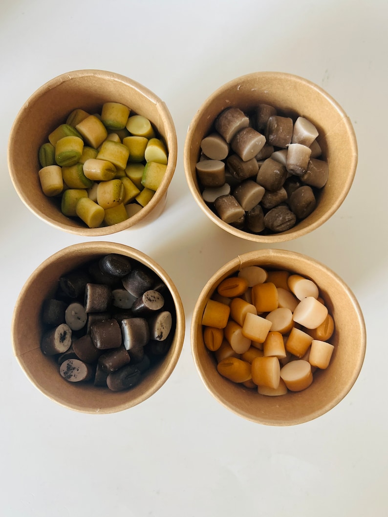May include: Four paper cups filled with different colored candy. The cups are arranged in a square pattern on a white surface. The candy is in various shapes and sizes.