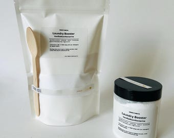 May include: A white pouch and a jar of laundry booster with the text "Laundry Booster VanillaBeanNectarine". Includes a wooden spoon. The pouch has a label with product information. The jar has a black lid.