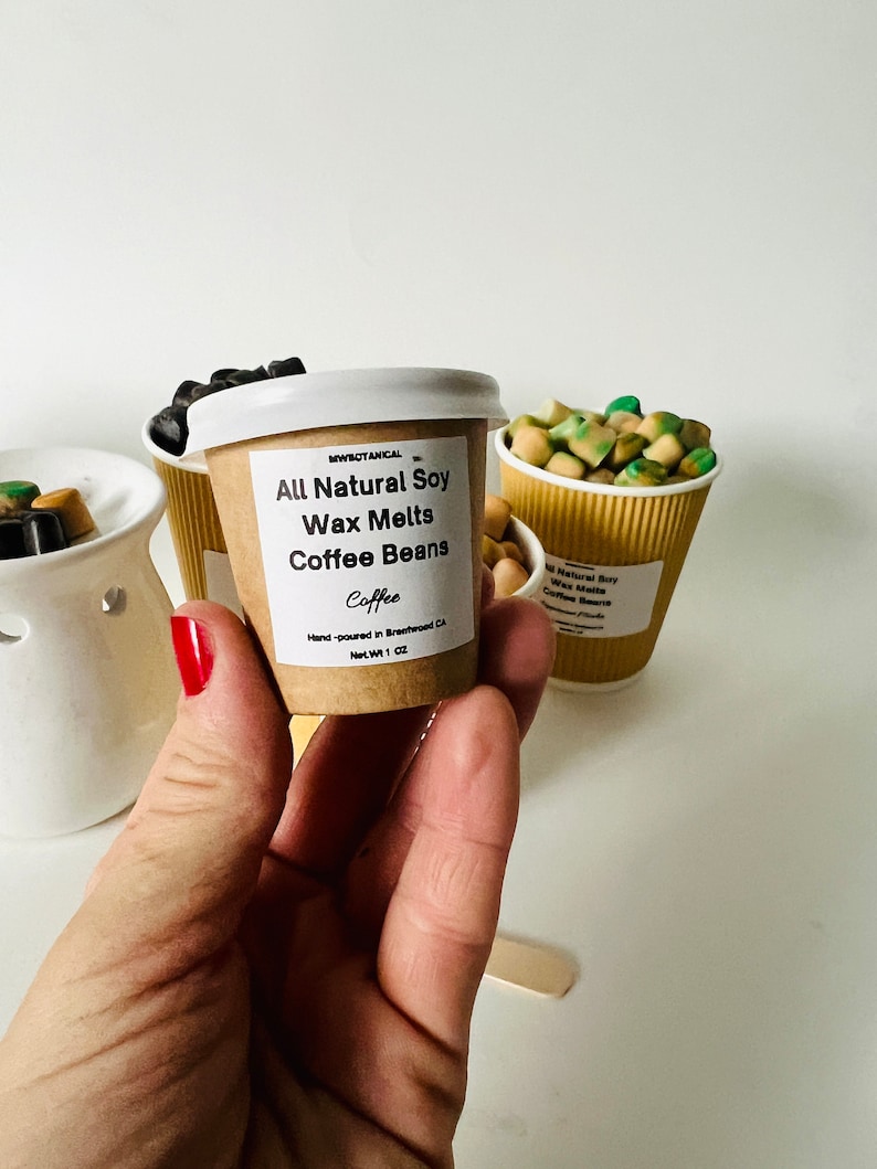 May include: A small brown paper cup filled with soy wax melts that smell like coffee. The label reads "All Natural Soy Wax Melts Coffee Beans Coffee" and "Hand-poured in Breawood, CA Net Wt 1 oz".