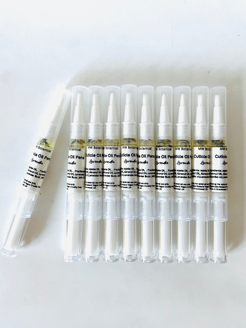 May include: A collection of cuticle oil pens with clear plastic tubes and white caps. The pens are filled with a light yellow liquid and small plant particles. The label reads "MW Botanical Cuticle Oil Pen" with "Lavender" below.