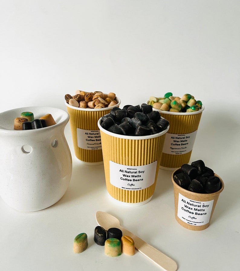May include: Assortment of coffee bean wax melts in brown paper cups. The wax melts are in various colors, including black, brown, and green. The cups have labels that say "All Natural Soy Wax Melts Coffee Beans".