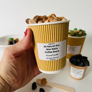 May include: A brown paper cup filled with coffee bean-shaped wax melts. The cup has a label that reads "All Natural Soy Wax Melts Coffee Beans Caramel Vanilla Hand-poured in Brentwood, CA Net Wt. 4 oz."