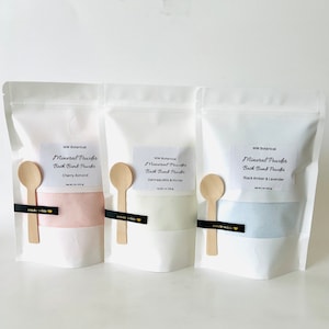 May include: Three white pouches with labels that read "Mineral Powder Bath Bomb Powder" in black text. The pouches contain different colored powders: pink, white, and blue. The pouches are labeled with different scents: Cherry Almond, Oatmeal Milk & Honey, and Black Amber & Lavender.