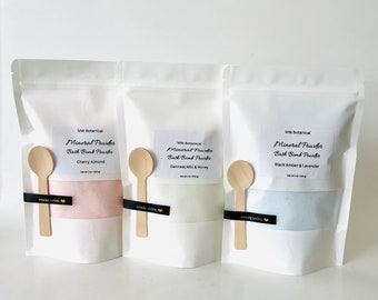 May include: Three white pouches with labels that read "Mineral Powder Bath Bomb Powder" in black text. The pouches contain different colored powders: pink, white, and blue. The pouches are labeled with different scents: Cherry Almond, Oatmeal Milk & Honey, and Black Amber & Lavender.