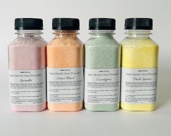 May include: Four bottles of bath bomb dust/powder in various colors: lavender, citrus blend, eucalyptus, and fresh lemons. Each bottle has a black cap and a label with the product name and ingredients.