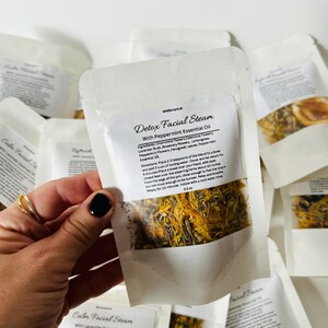 May include: A white paper pouch with a label that reads "Detox Facial Steam with Peppermint Essential Oil". The pouch contains a blend of dried herbs and flowers, including chamomile, calendula, lavender, rosemary, lemongrass, fenugreek, and peppermint. The pouch is 0.5 oz.