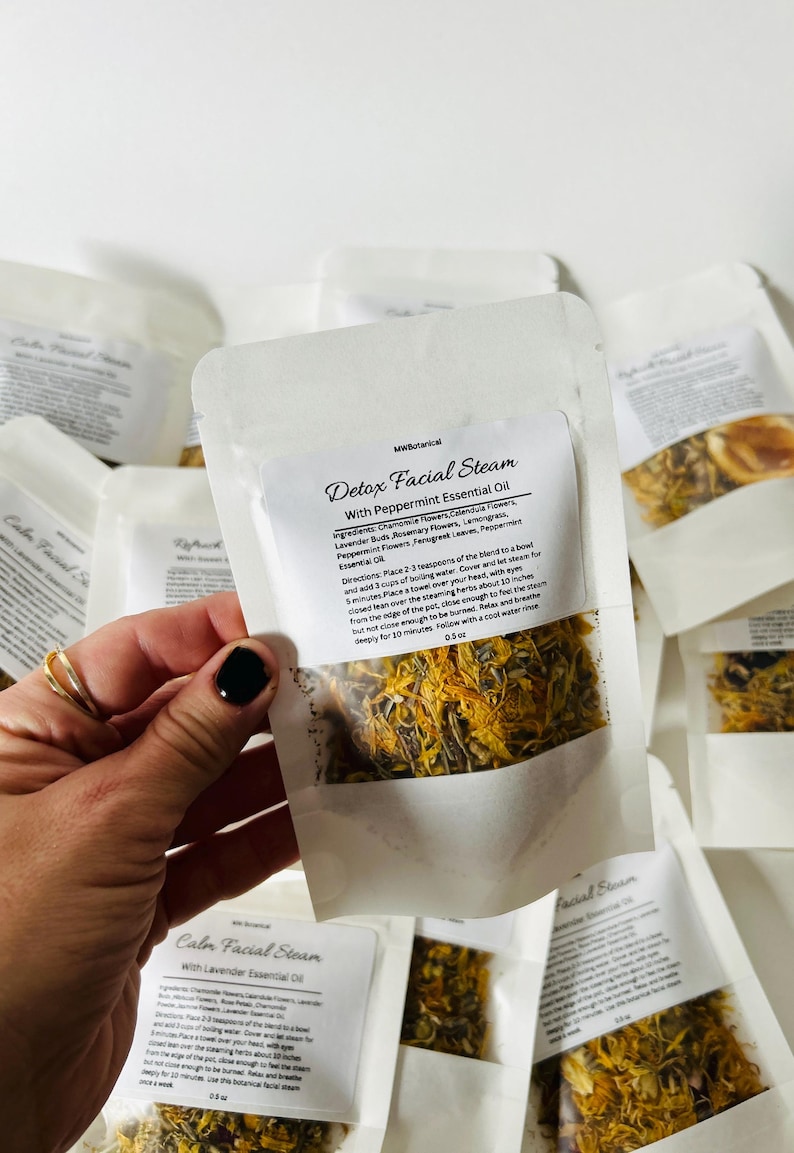 May include: A white paper pouch with a label that reads "Detox Facial Steam with Peppermint Essential Oil". The pouch contains a blend of dried herbs and flowers, including chamomile, calendula, lavender, rosemary, lemongrass, fenugreek, and peppermint. The pouch is 0.5 oz.