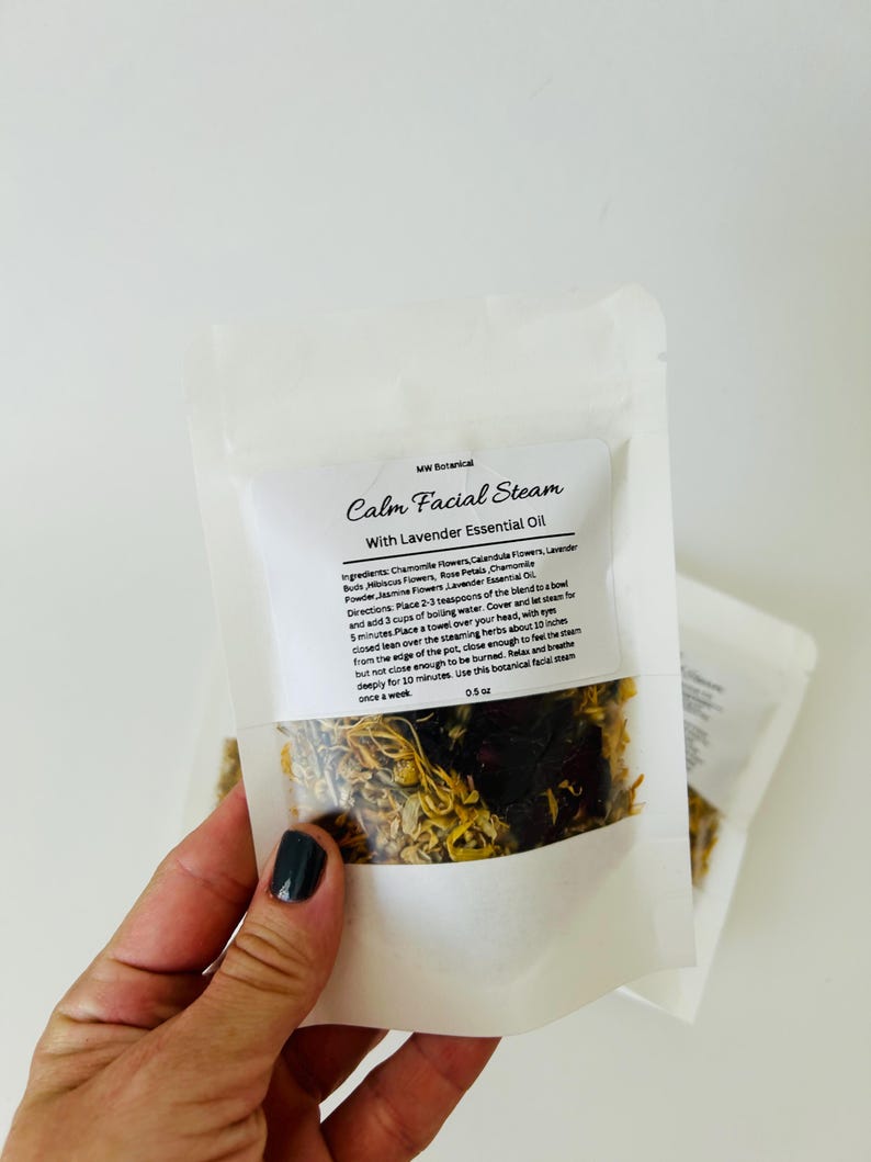 May include: A white pouch with a clear window showing a blend of dried herbs and flowers. The pouch is labeled "Calm Facial Steam with Lavender Essential Oil". The ingredients are listed as chamomile flowers, calendula flowers, lavender buds, hibiscus flowers, rose petals, chamomile powder, and jasmine flowers. The directions for use are also included.
