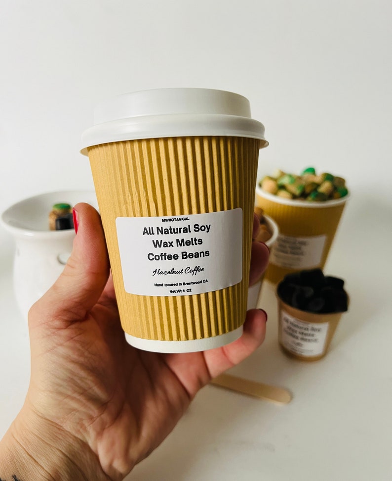 May include: A brown paper cup with a white lid filled with soy wax melts. The label reads "MWBOTANICAL All Natural Soy Wax Melts Coffee Beans Hazelnut Coffee Hand-poured in Brentwood CA Net Wt 4 OZ".