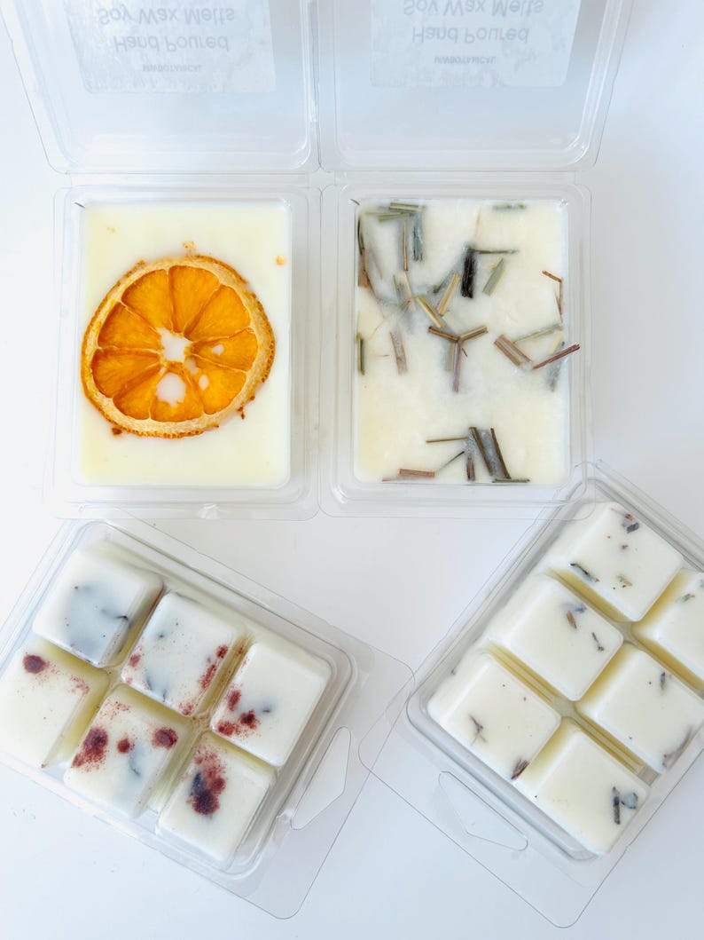 May include: Four clear plastic clamshell containers filled with off-white soy wax melts. One container features a dried orange slice, another contains dried lemongrass, and two containers hold segmented wax cubes with botanical inclusions.