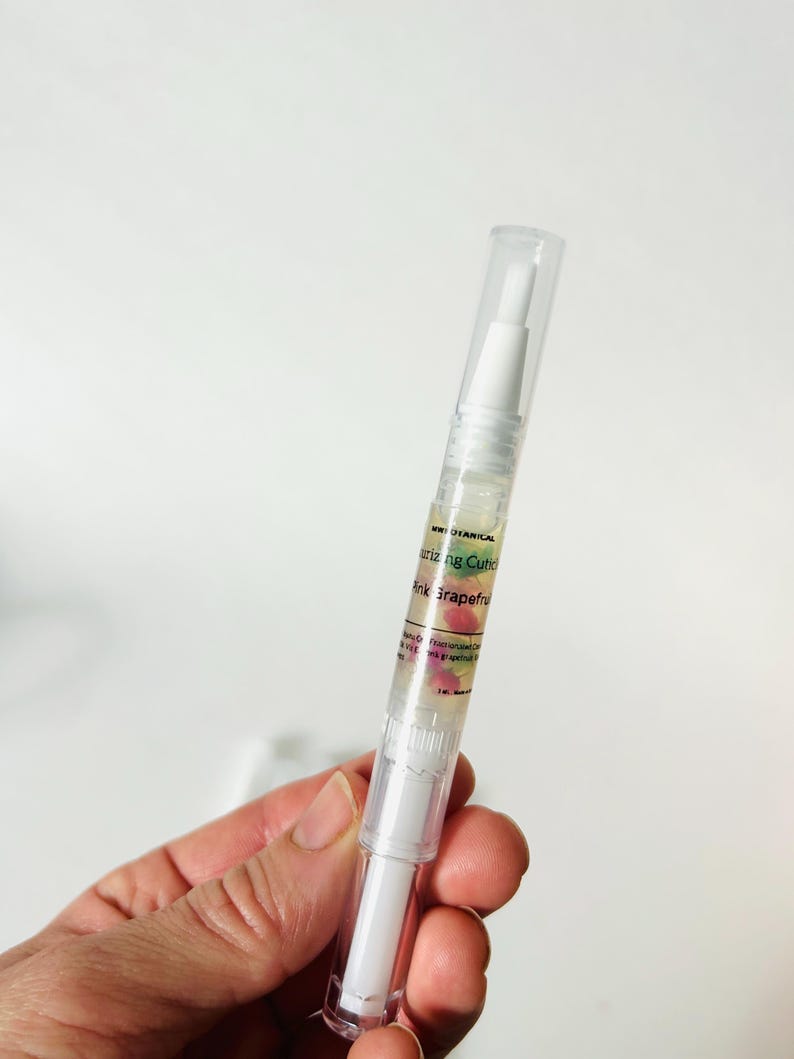May include: A clear cuticle oil pen with a white applicator tip and a clear cap. The pen has a label with the text "Botanical" and "Pink Grapefruit". The oil contains pink grapefruit pieces.